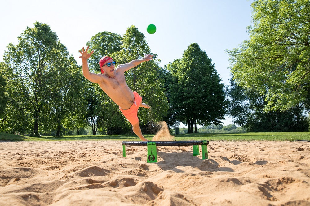 Ein Roundnet Spieler am Strand im Sprungflug, um den Ball zu schlagen