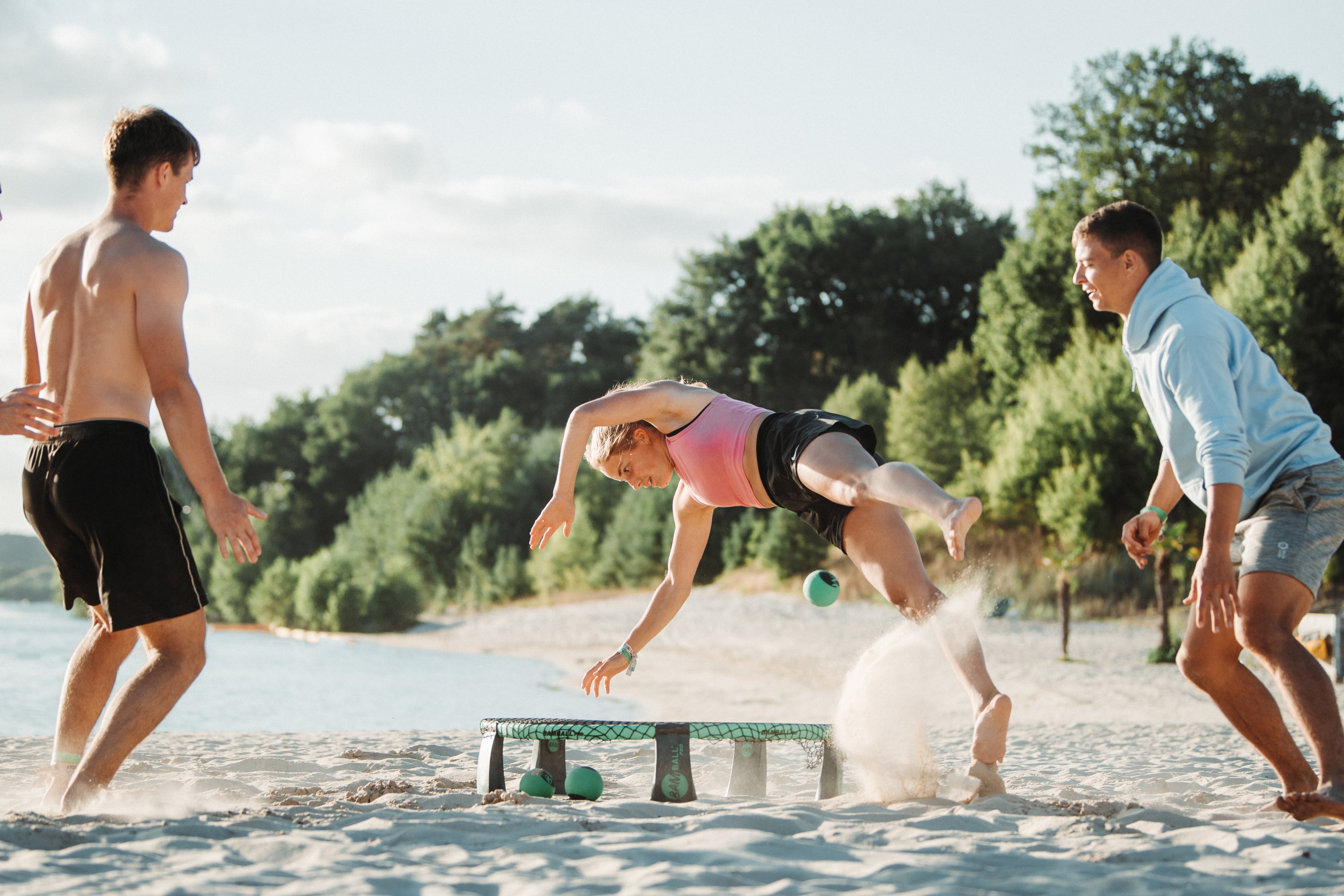 Drei Roundnet Spieler auf Sand, eine Spielerin in der Luft, um den Ball aufs Netz zu schlagen
