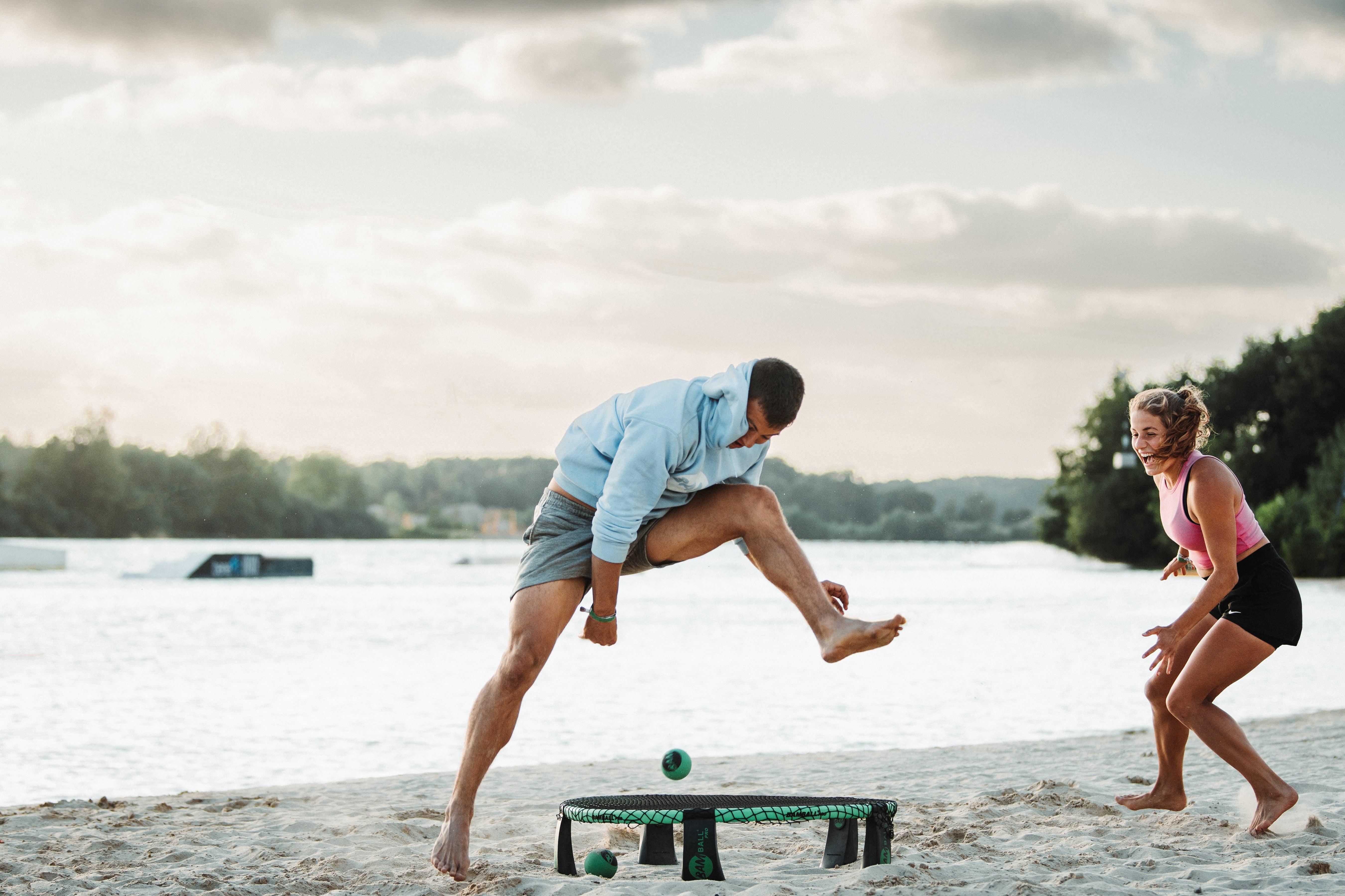 Zwei Roundnet Spieler auf dem Sand, der eine spielt den Ball zwischen seine Beine aufs Netz
