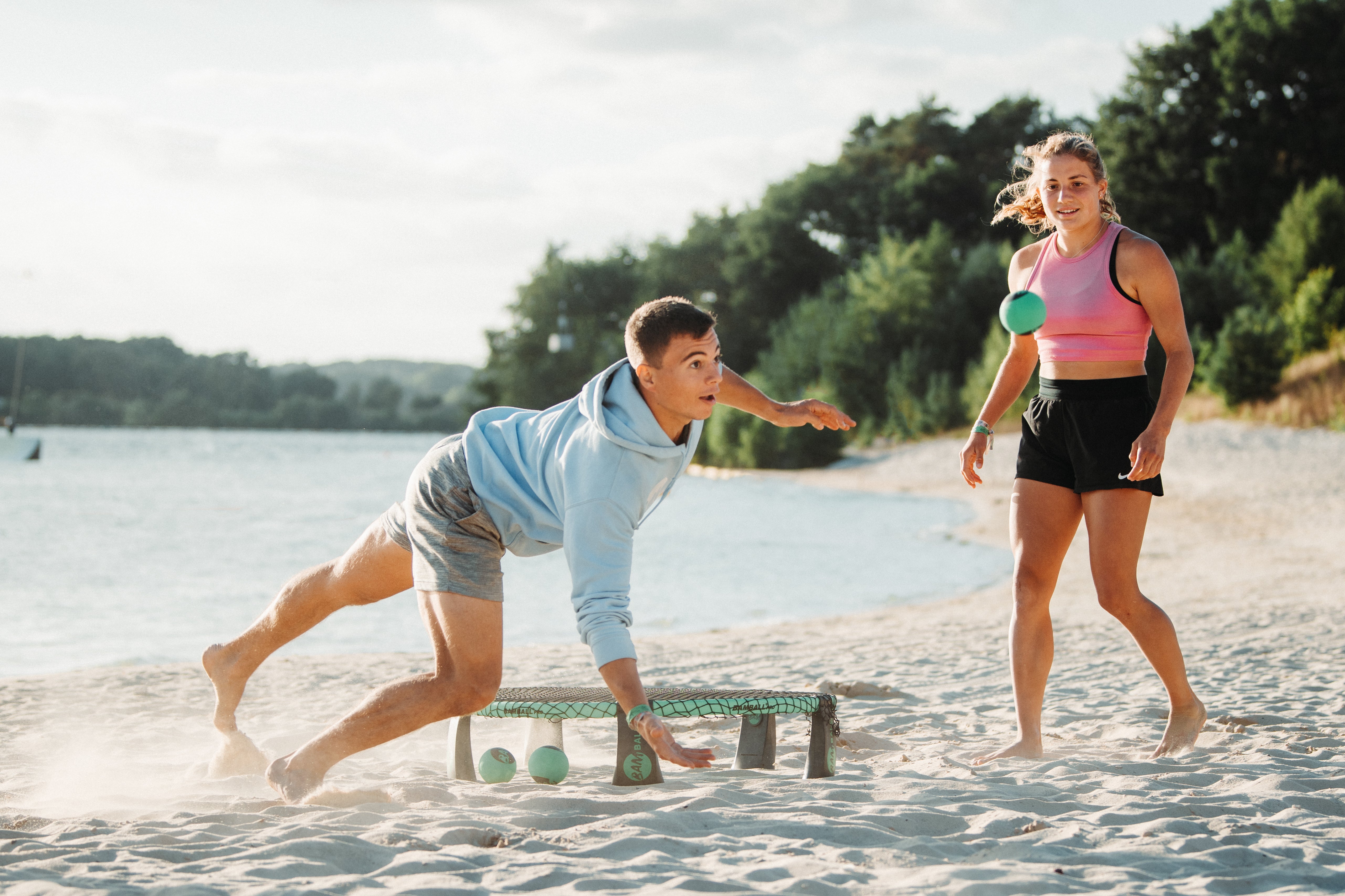 zwei Roundnet Spieler im Sand, wobei ein Spieler den Ball durch einen Sprung noch erreichen will