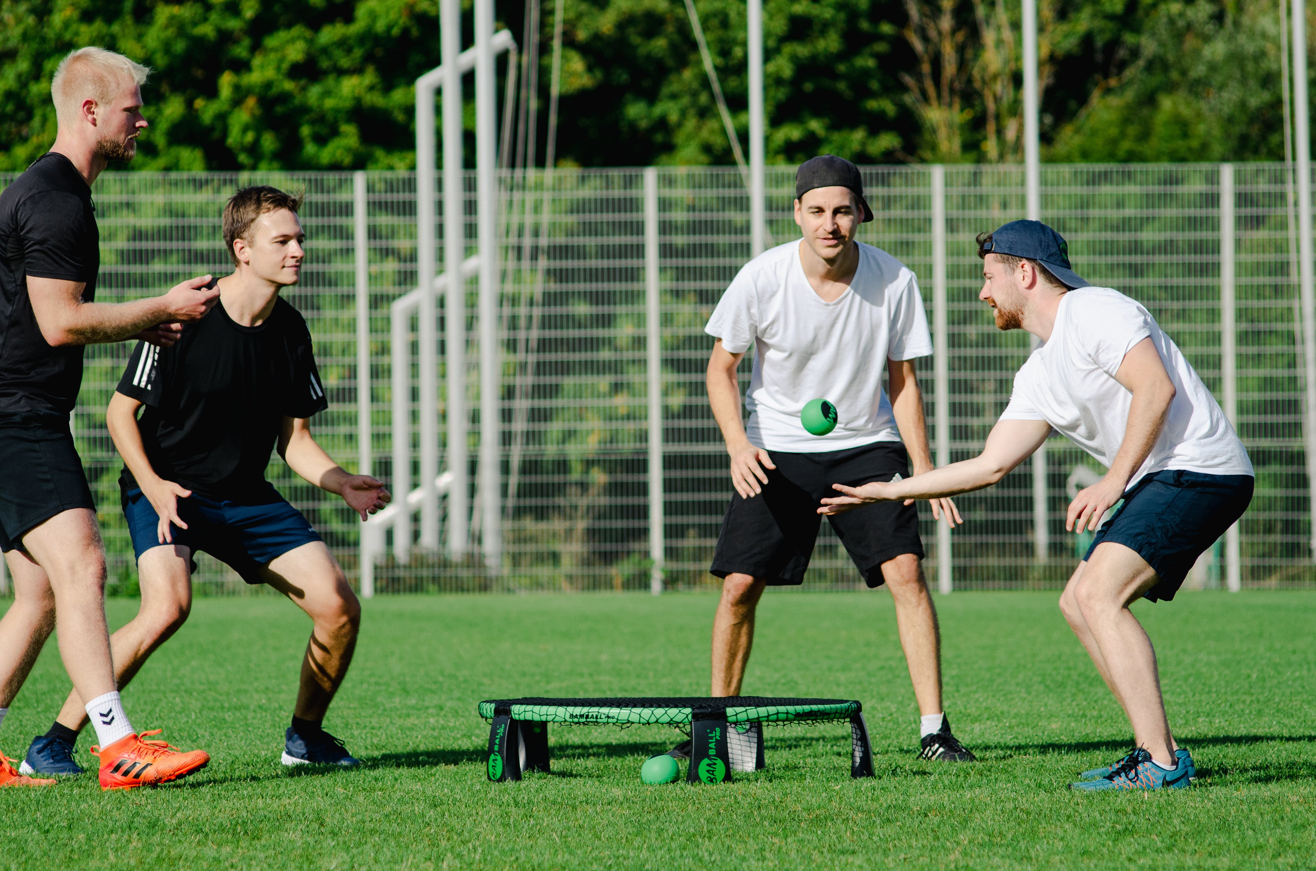 Vier Roundnet Sportler auf Gras, ein Spieler ist kurz davor, den Ball für seinen Mitspieler zu stellen