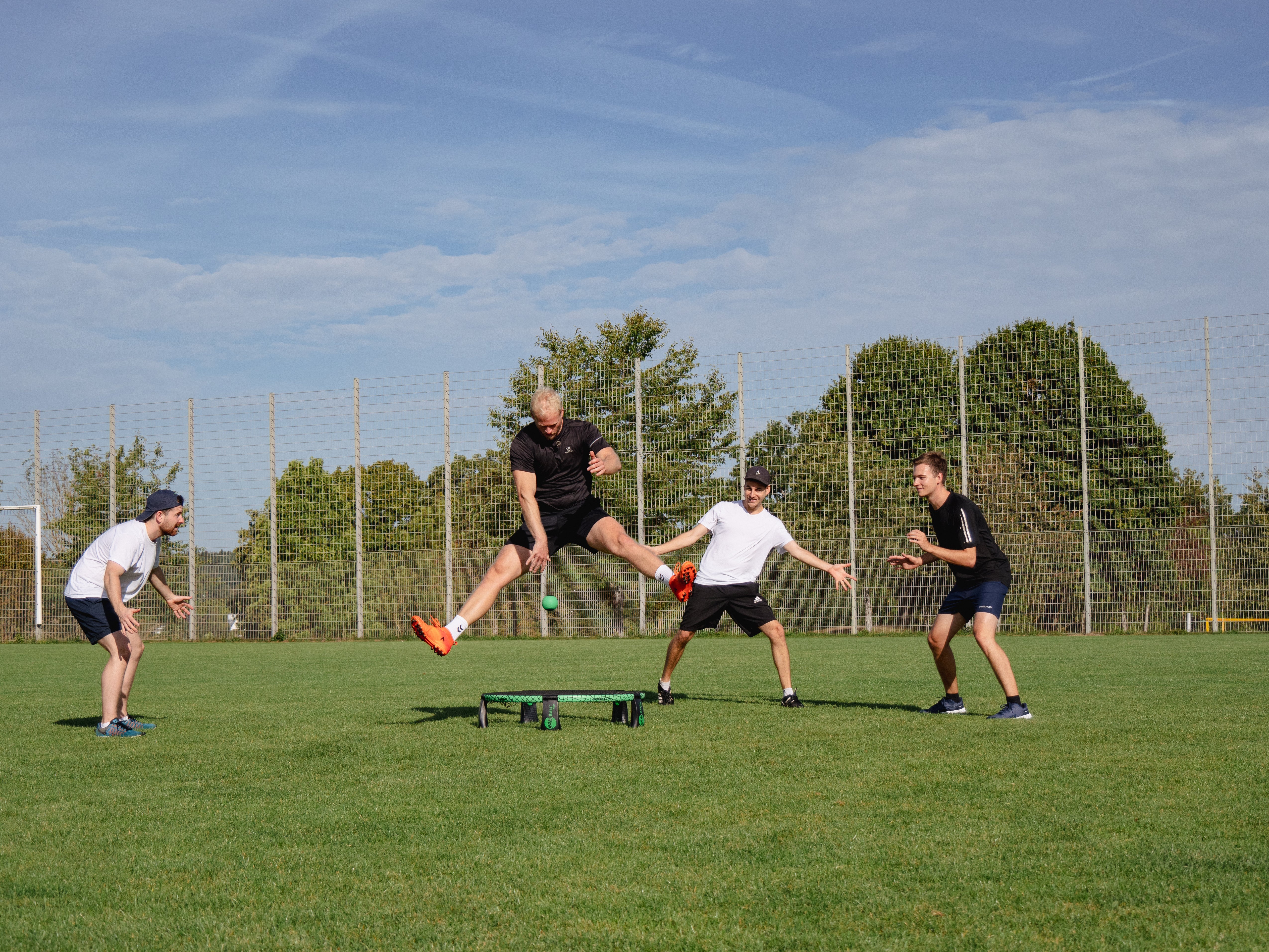 Roundnet Spiel, Spieler springt übers Netz und schlägt den Ball zwischen die Beine