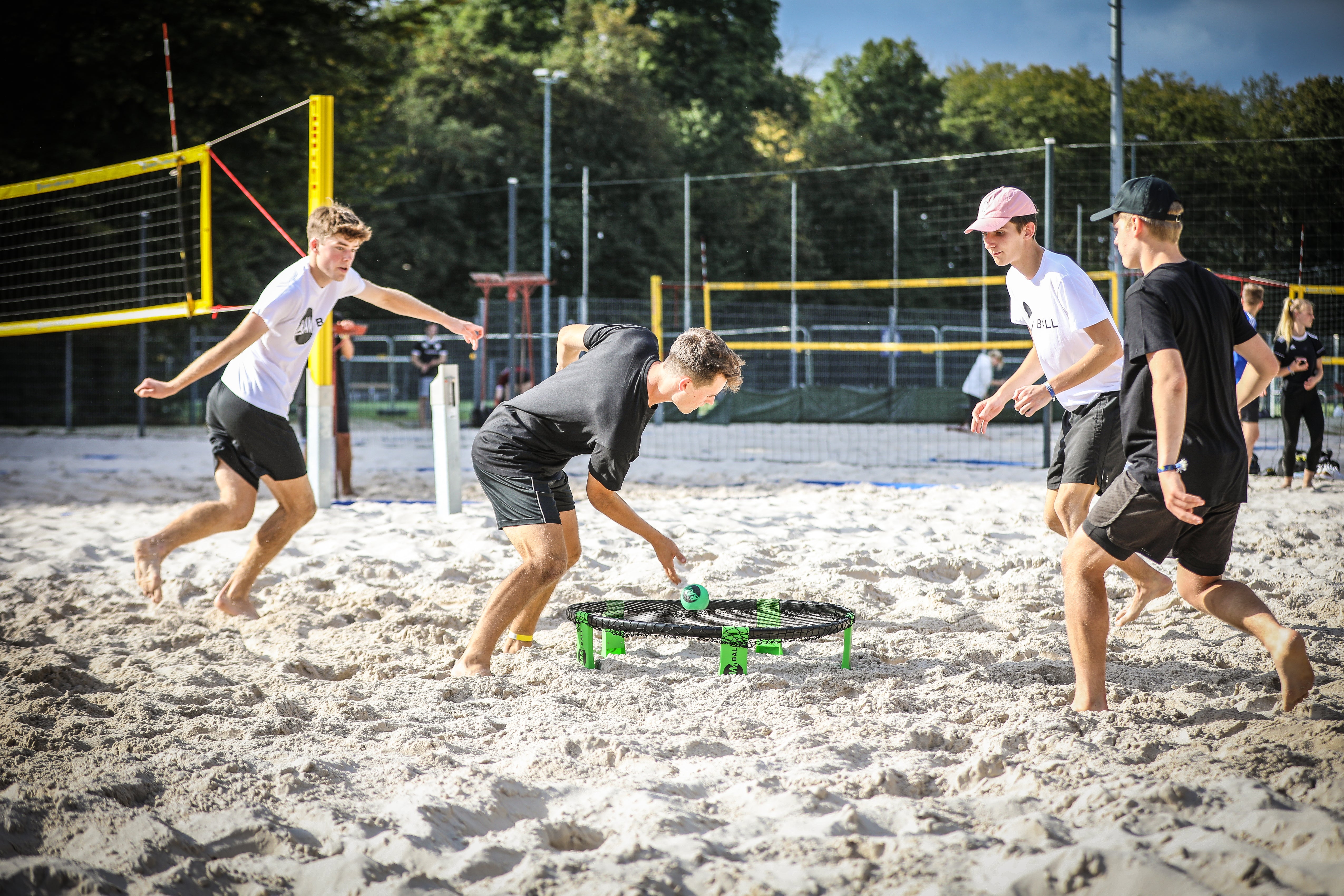 Vier Roundnet Spieler auf Sand, ein Sportler spielt einen kurzen Ball aufs Netz